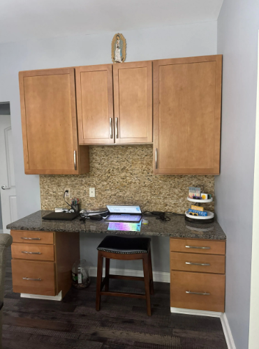 Desk with cabinets, drawers, granite countertop, and backsplash. A stool sits underneath the desk.
