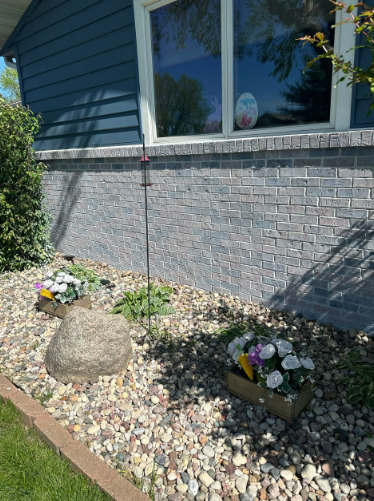 A house with a blue facade, a window, and a small rock garden with flowers.