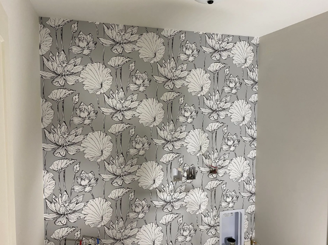 Gray wallpaper with large white lotus flower pattern on a wall, with unfinished electrical fixtures.