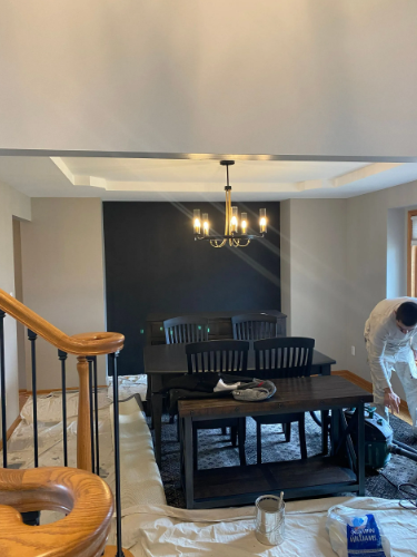 Dining room: black accent wall, table and chairs, chandelier, person in painting clothes.