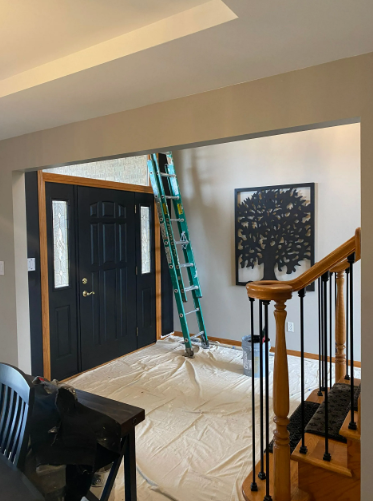 An interior doorway with a black door, ladder, and tree artwork on the wall. Painting in progress, floor covered.