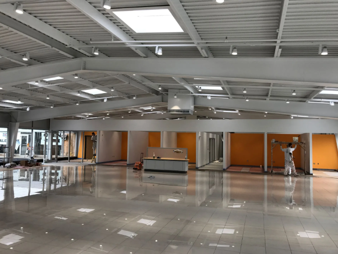 Large, empty interior space under construction; white walls, orange accent walls, and reflective floor.