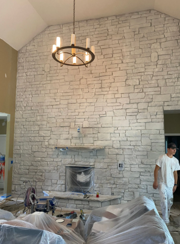Stone accent wall with a fireplace and a chandelier. A person stands nearby.