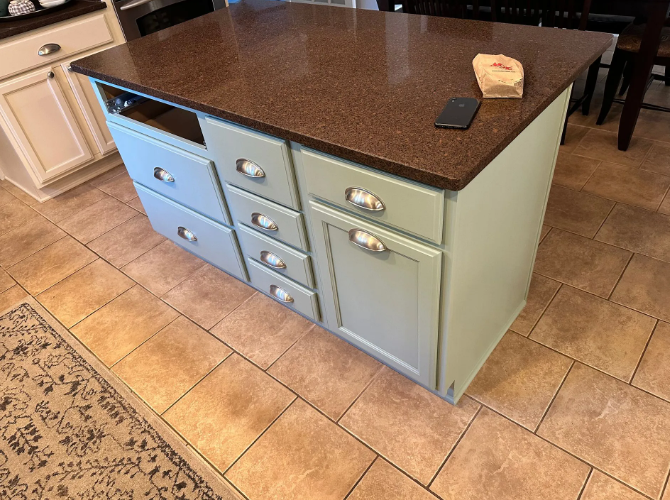 Kitchen island with brown countertop, teal cabinets, and drawers.