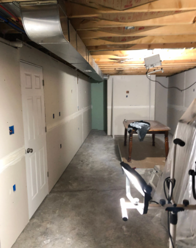 Basement with drywall, ductwork, a door, and exercise equipment. Concrete floor.