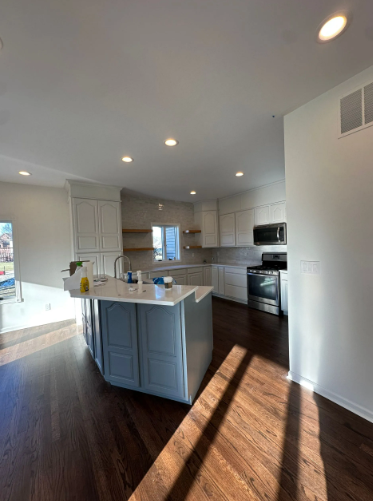 Kitchen with blue island, white cabinets, stainless steel appliances, and dark wood floors.