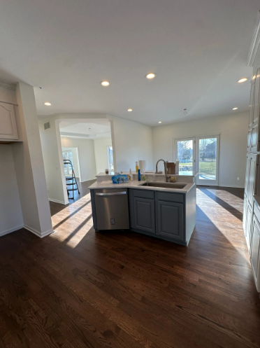 Kitchen with blue island, sink, dishwasher, and dark wood floors. White walls and lots of natural light.
