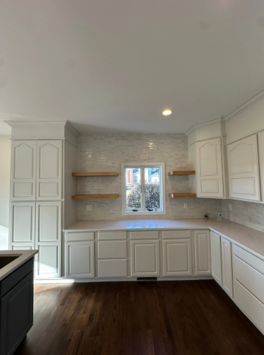 White kitchen with cabinets, open shelves, and window above countertop with dark wood floor.
