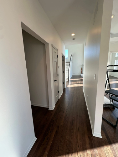 Hallway with dark wood floors, white walls, and doors leading to rooms. Stairs at the end.