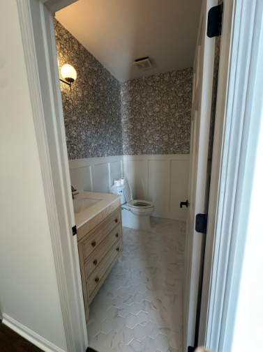 Small powder room with floral wallpaper, white wainscoting, hexagon tile floor, and a vanity.