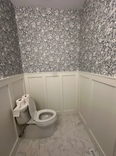 Small bathroom with floral wallpaper, white wainscoting, and a toilet.