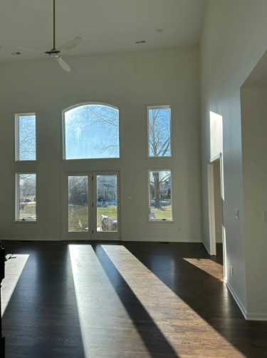 Large, sunlit room with dark wood floor, tall windows, and white walls.