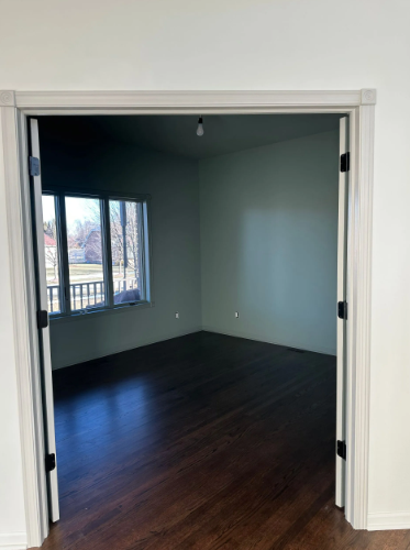 Interior view of a room with dark wood floors, light green walls, and a window. Seen through a doorway.