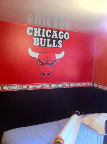 Chicago Bulls logo on a red wall, above a bed with a blue sheet.