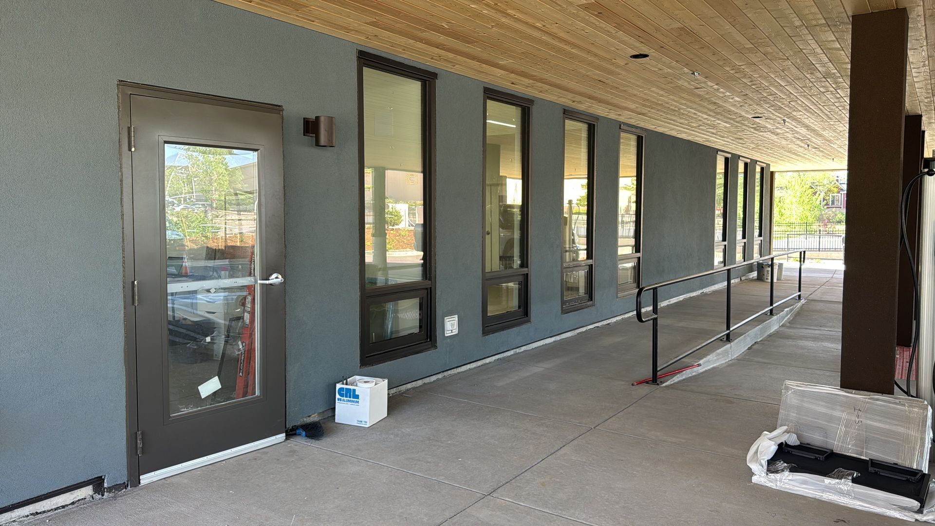 Exterior of building with a long, covered walkway, gray wall, dark windows, and a ramp.