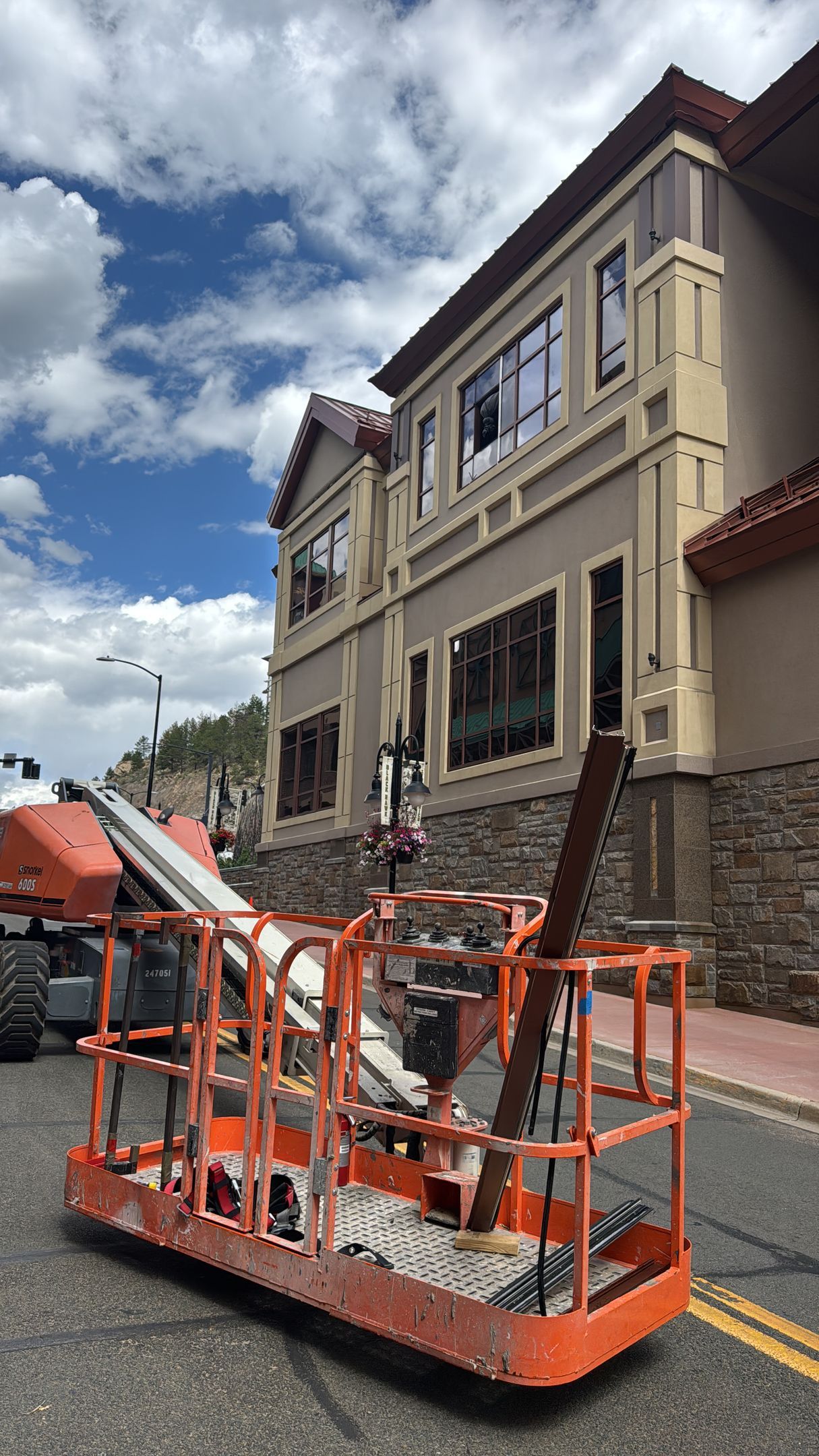Orange lift in front of a building with brown and beige exterior, street setting, work being done.