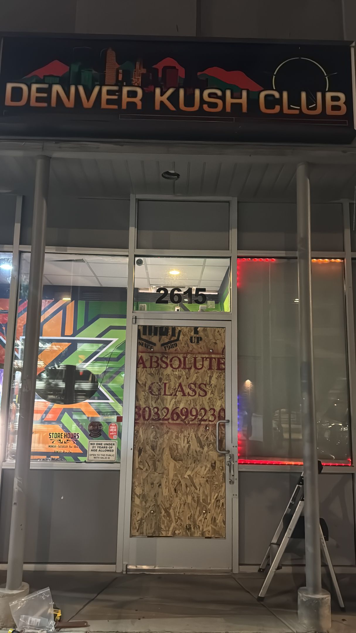 Denver Kush Club storefront with boarded-up door, graffiti art, and neon sign.