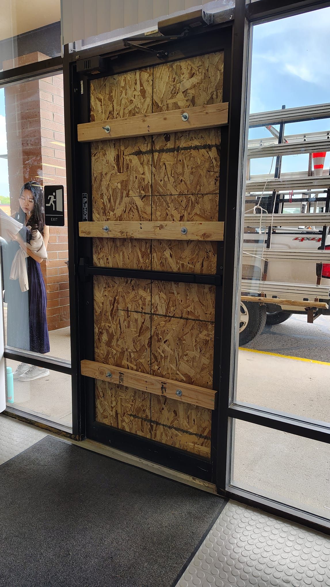 Boarded-up doorway at a building entrance, featuring plywood and wood supports. A person stands inside.