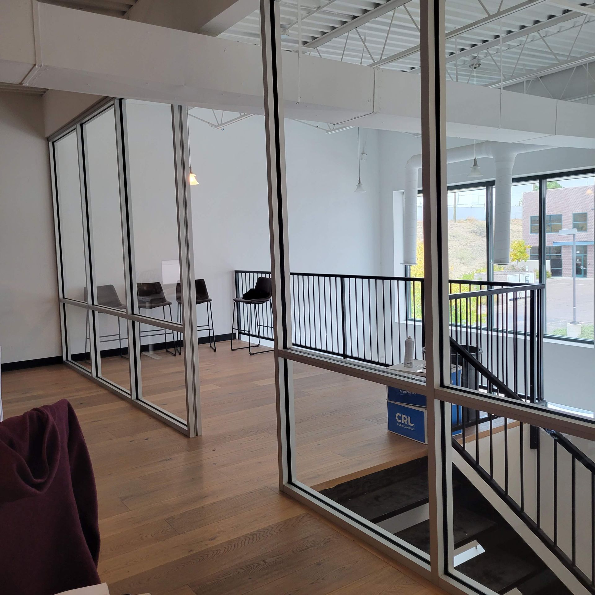 Modern office interior with glass walls, wooden floors, and a second-floor balcony.