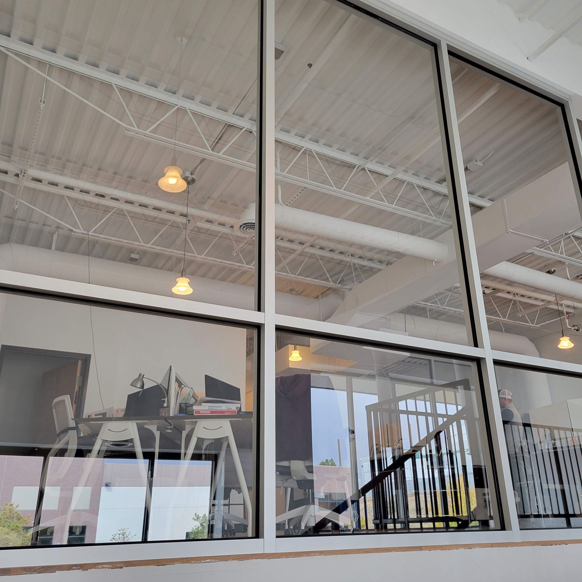 Large glass windows overlooking a modern office interior with a staircase and desks.