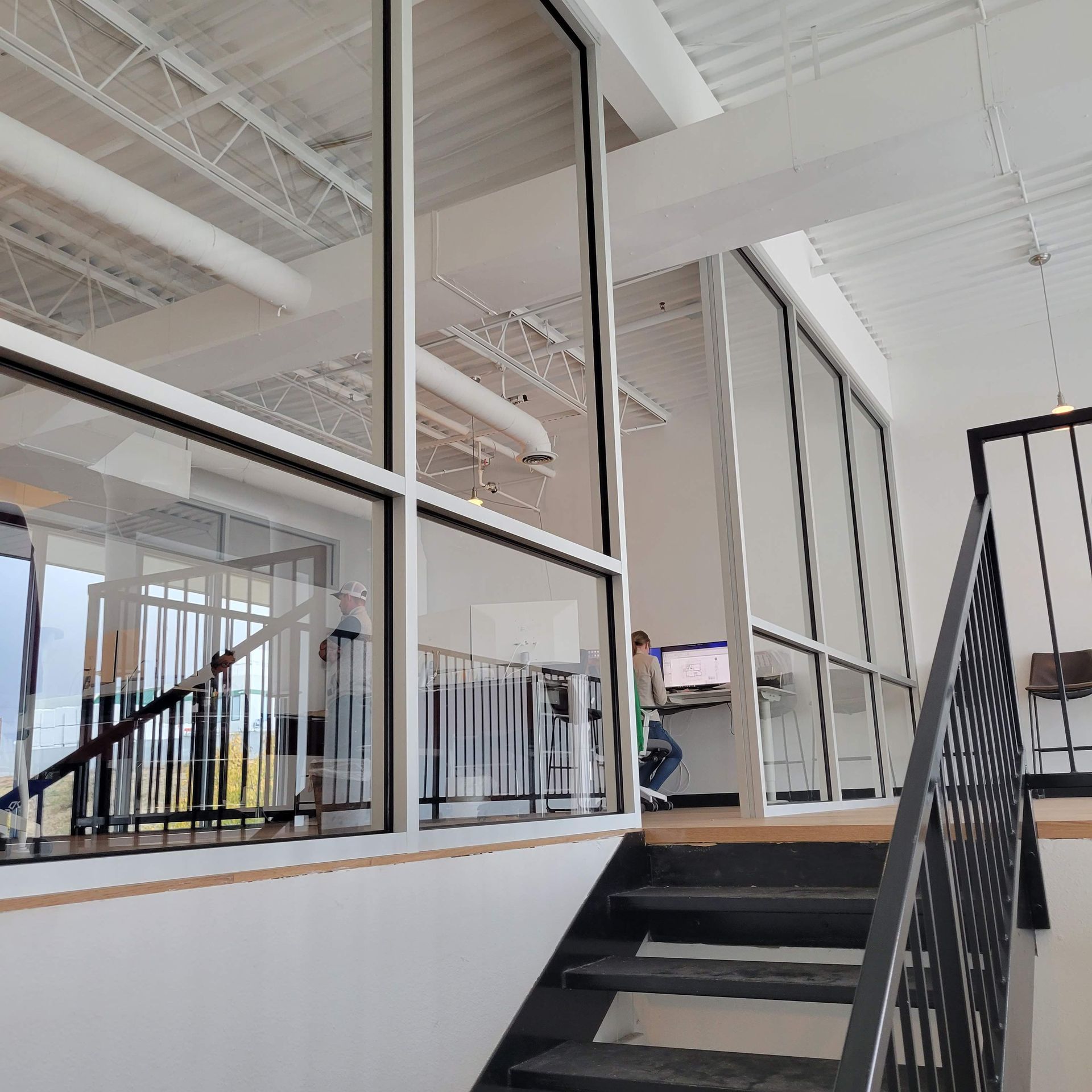 Staircase leading up to a glass-walled office space with a person working at a desk.