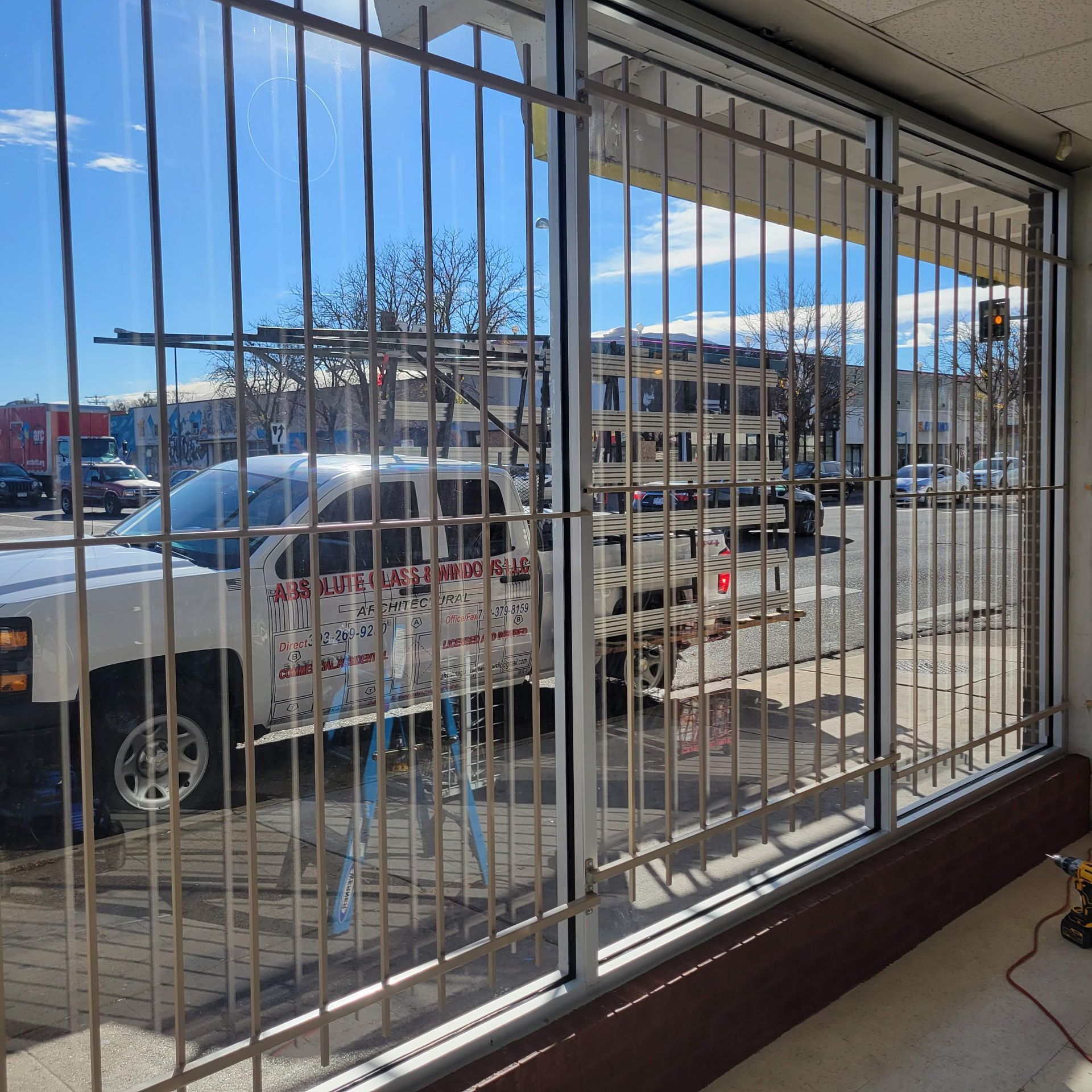 Security bars on windows of a store with a white truck parked outside. Blue sky.