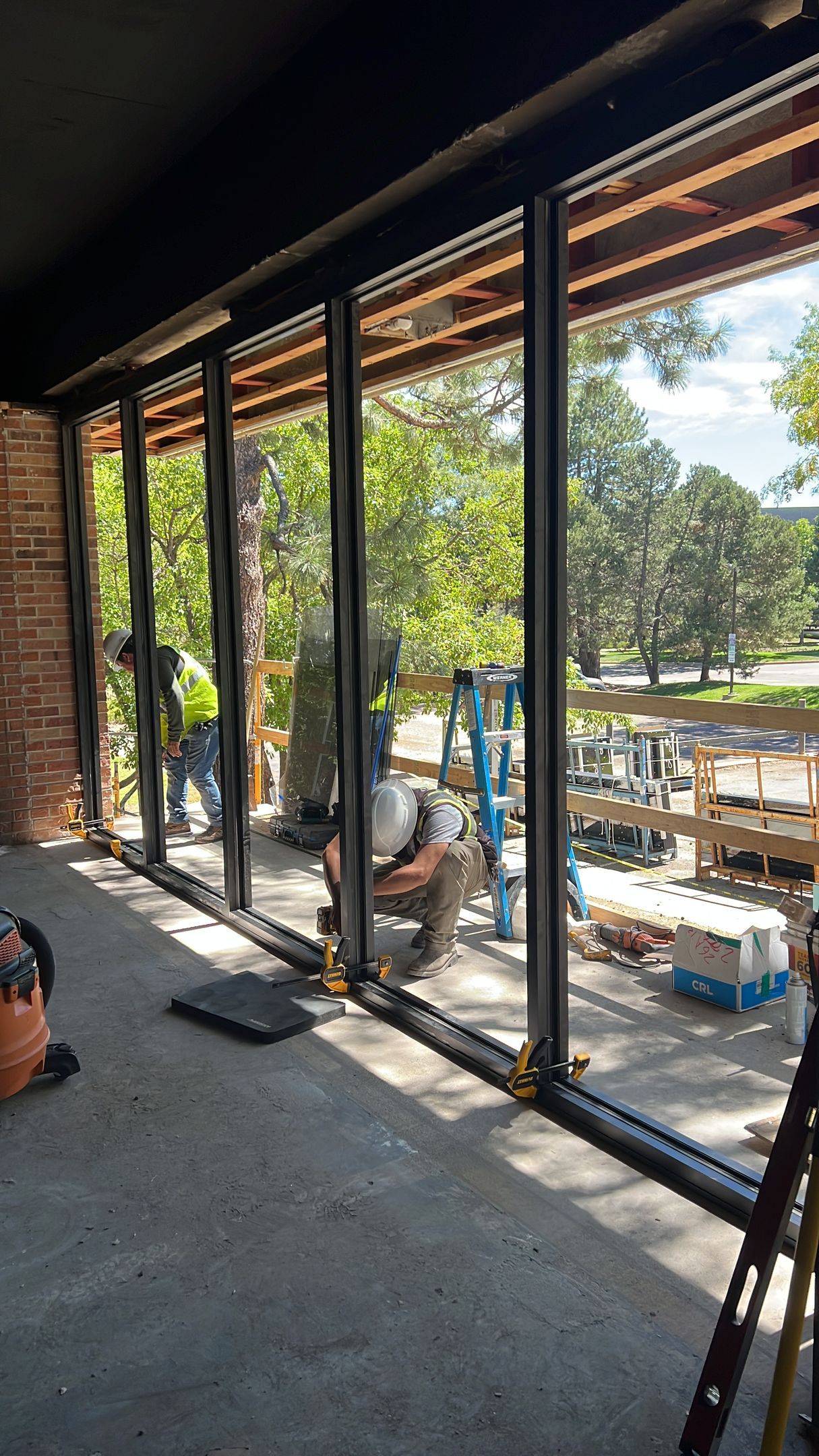 Person installing glass doors, visible outdoor setting with trees.