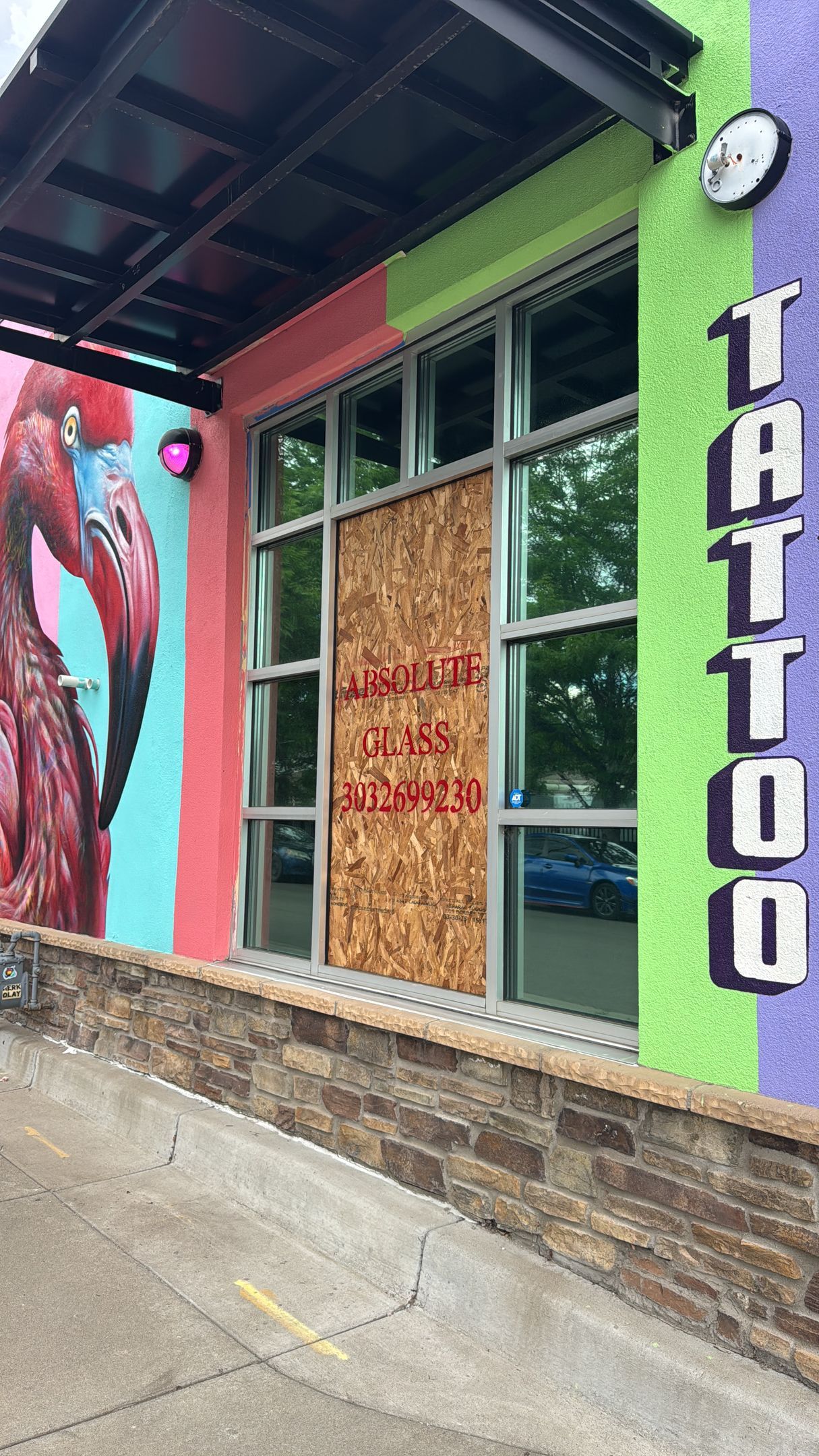 Tattoo shop exterior with boarded-up window; colorful mural, pink, green, purple paint.