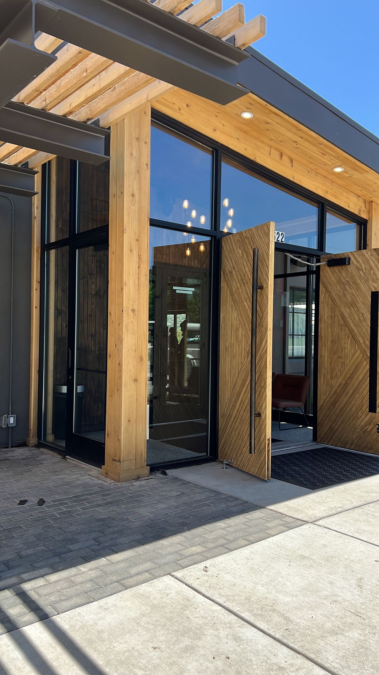 Modern building entrance with wood and glass, open door, sunny day.