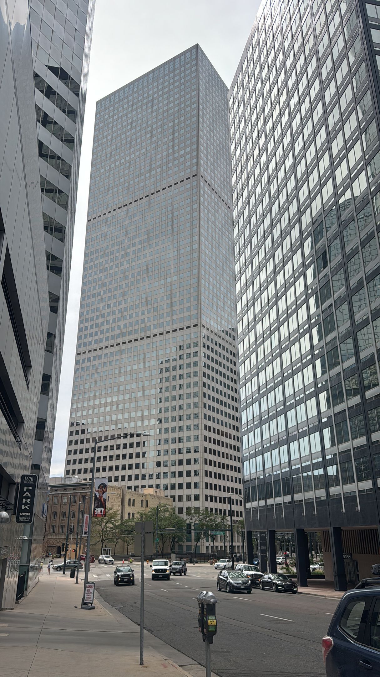 Tall glass skyscraper between two other buildings on a city street with cars.