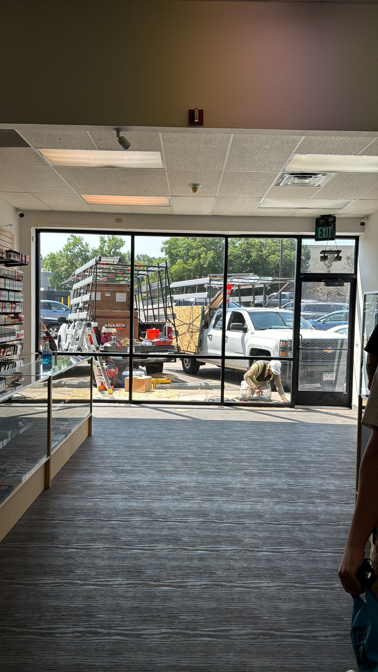View through a store front window of a parking lot and people; daylight.