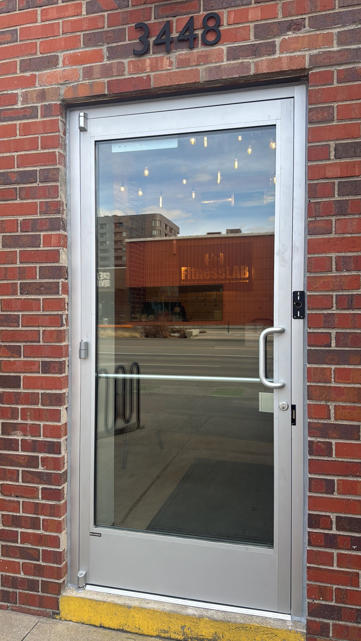 Silver-framed glass door in a brick building. Exterior view with building number 3448 above the door.