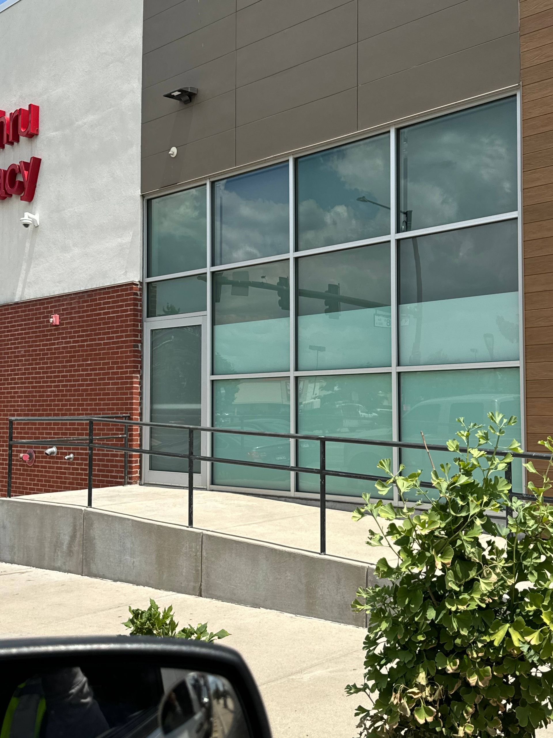 Exterior of a building with large windows, a door, and a ramp. Brick and gray siding. Black railings.