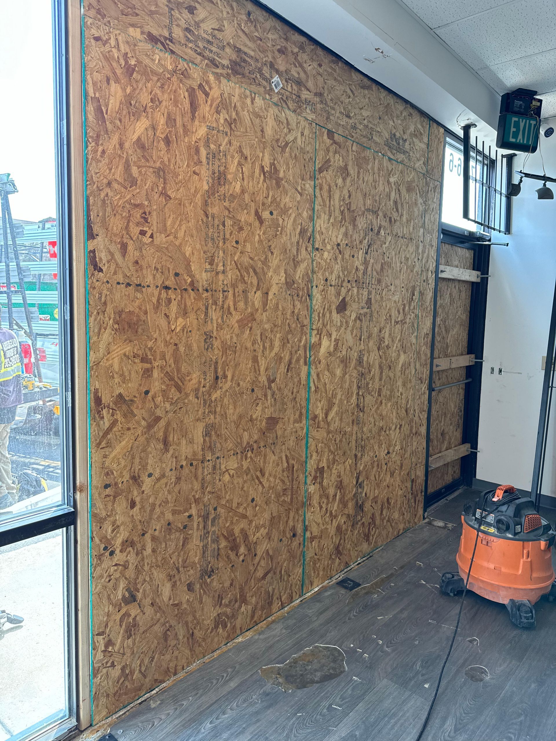 Wood-paneled storefront, possibly boarded up, with a partial view of a cityscape outside.  A shop vacuum sits nearby.