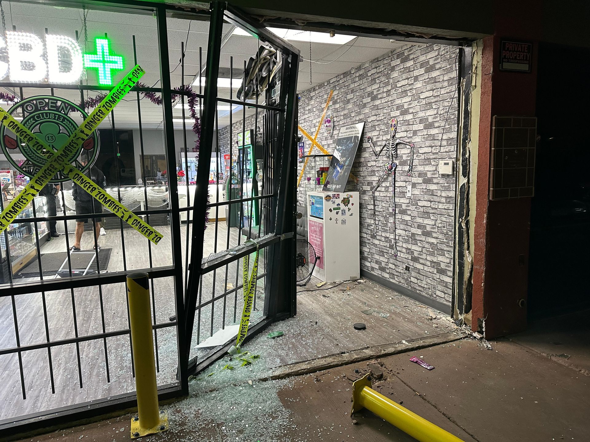 Night view of a smashed CBD store entrance; broken glass and metal gate, caution tape.