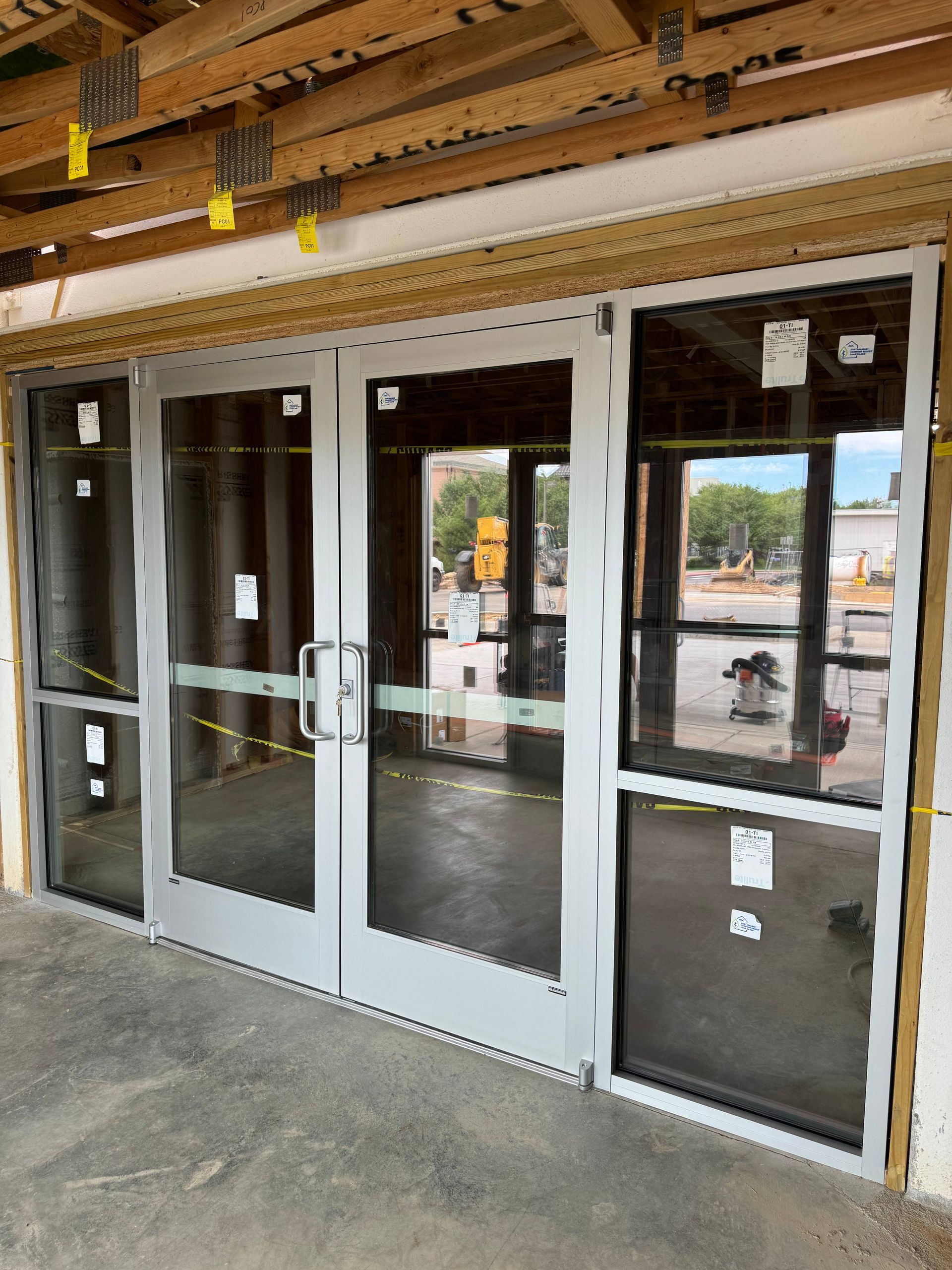 Exterior view of newly installed double doors with glass panels, under construction.