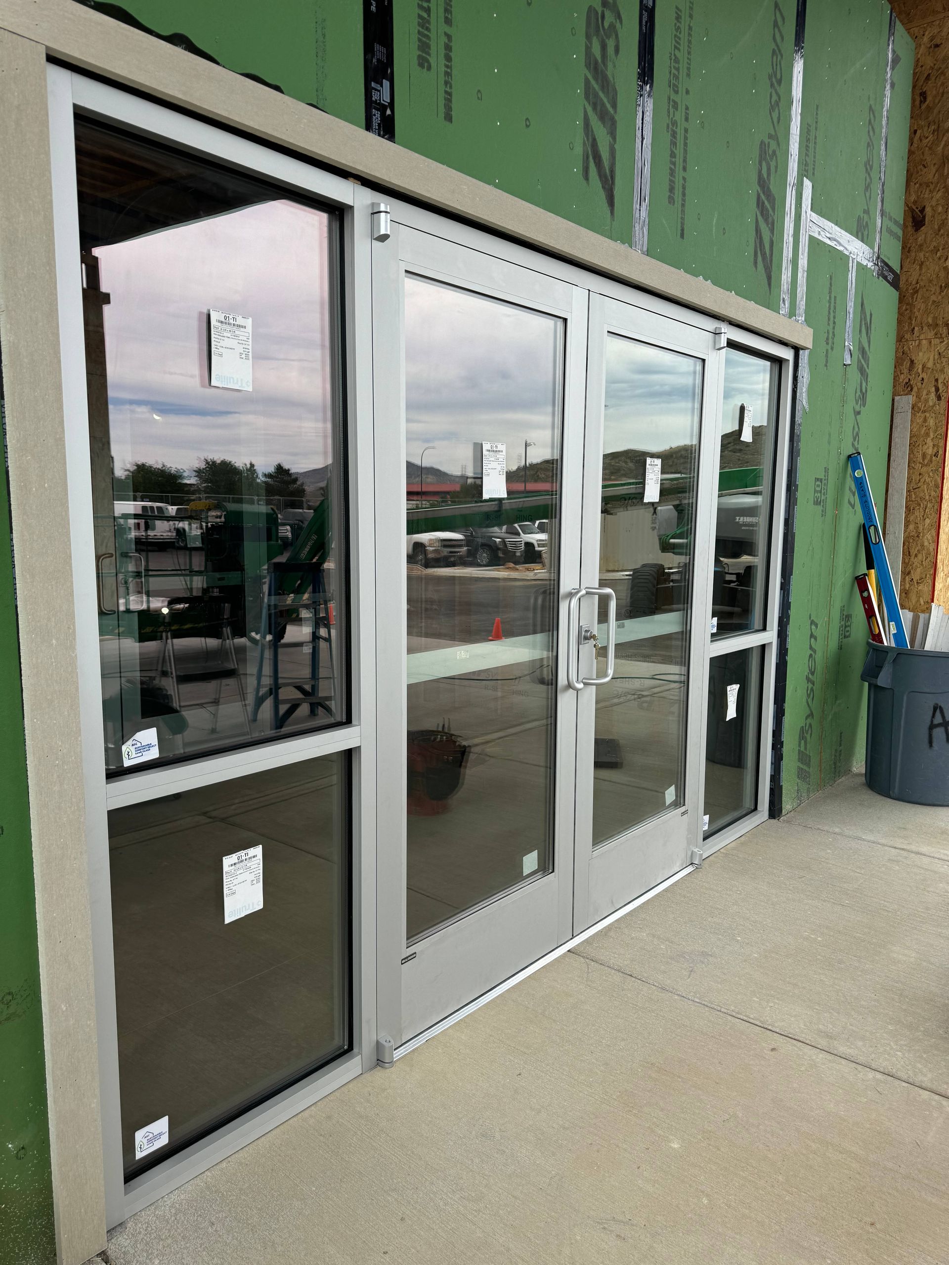 Glass storefront doors with silver frames, under construction.
