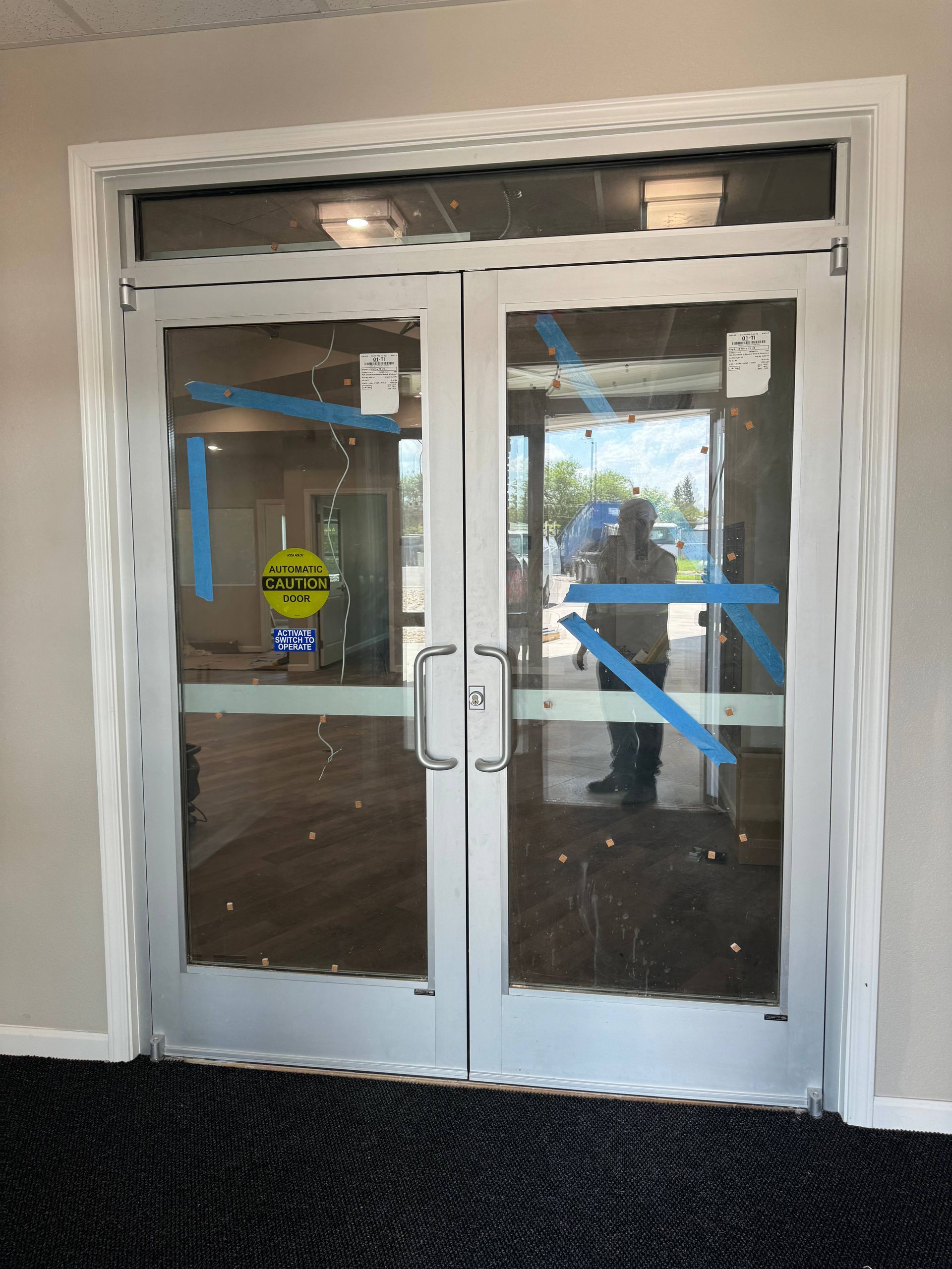 Double glass doors with blue tape, automatic door sign, and silver frames in a building.