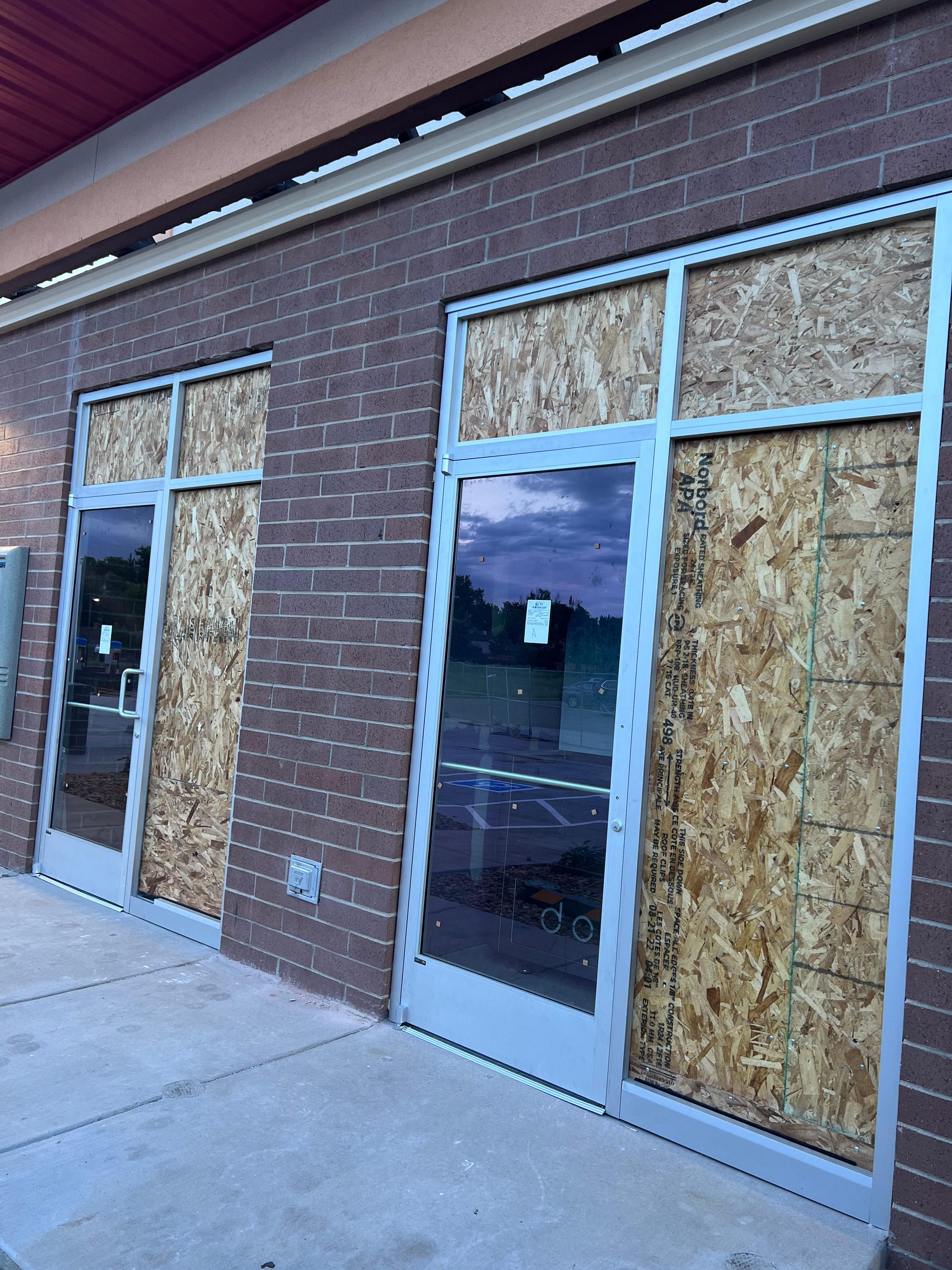 Exterior of a brick building with plywood covering glass doors and windows.
