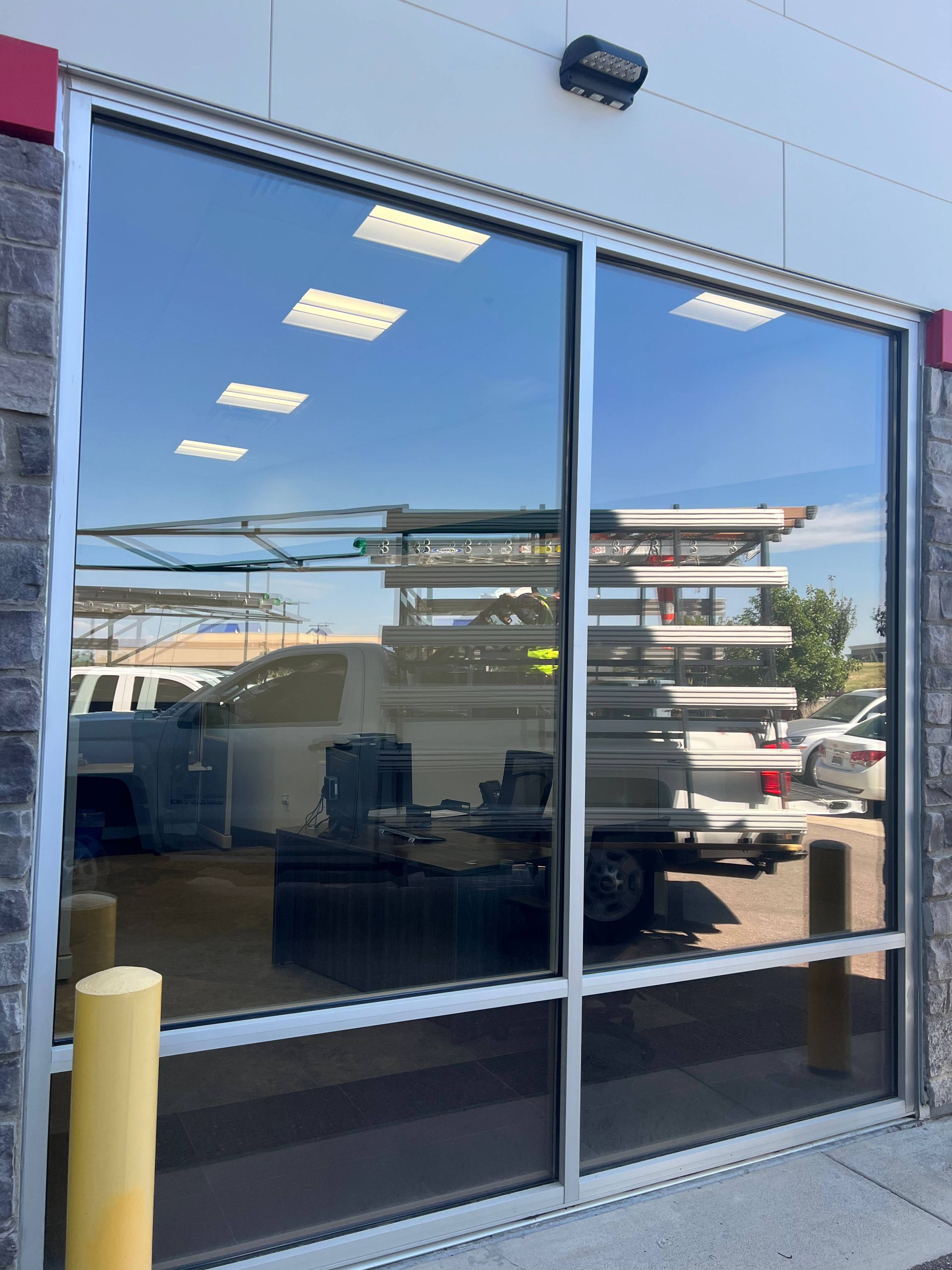 Large windows with reflective tint on a building, reflecting blue sky and service vehicles.