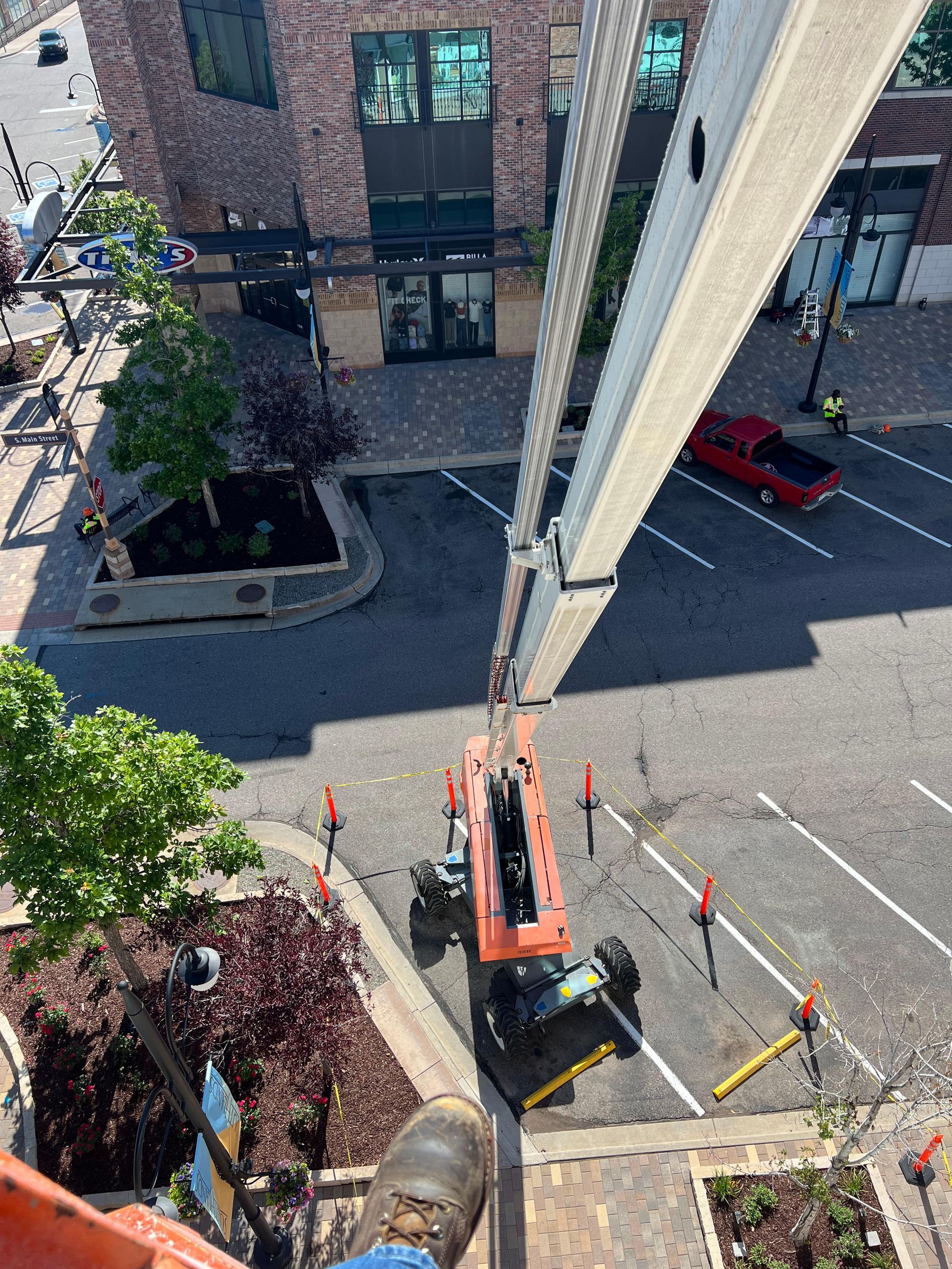 View from above of a construction lift arm.  Street below; red truck parked. Brick building in background.