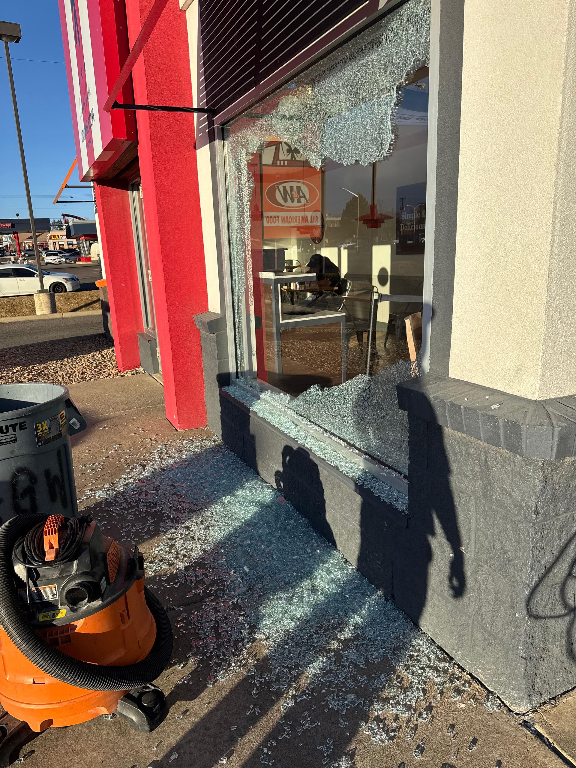 Shattered storefront window with glass debris on the ground; an orange shop vac sits nearby.