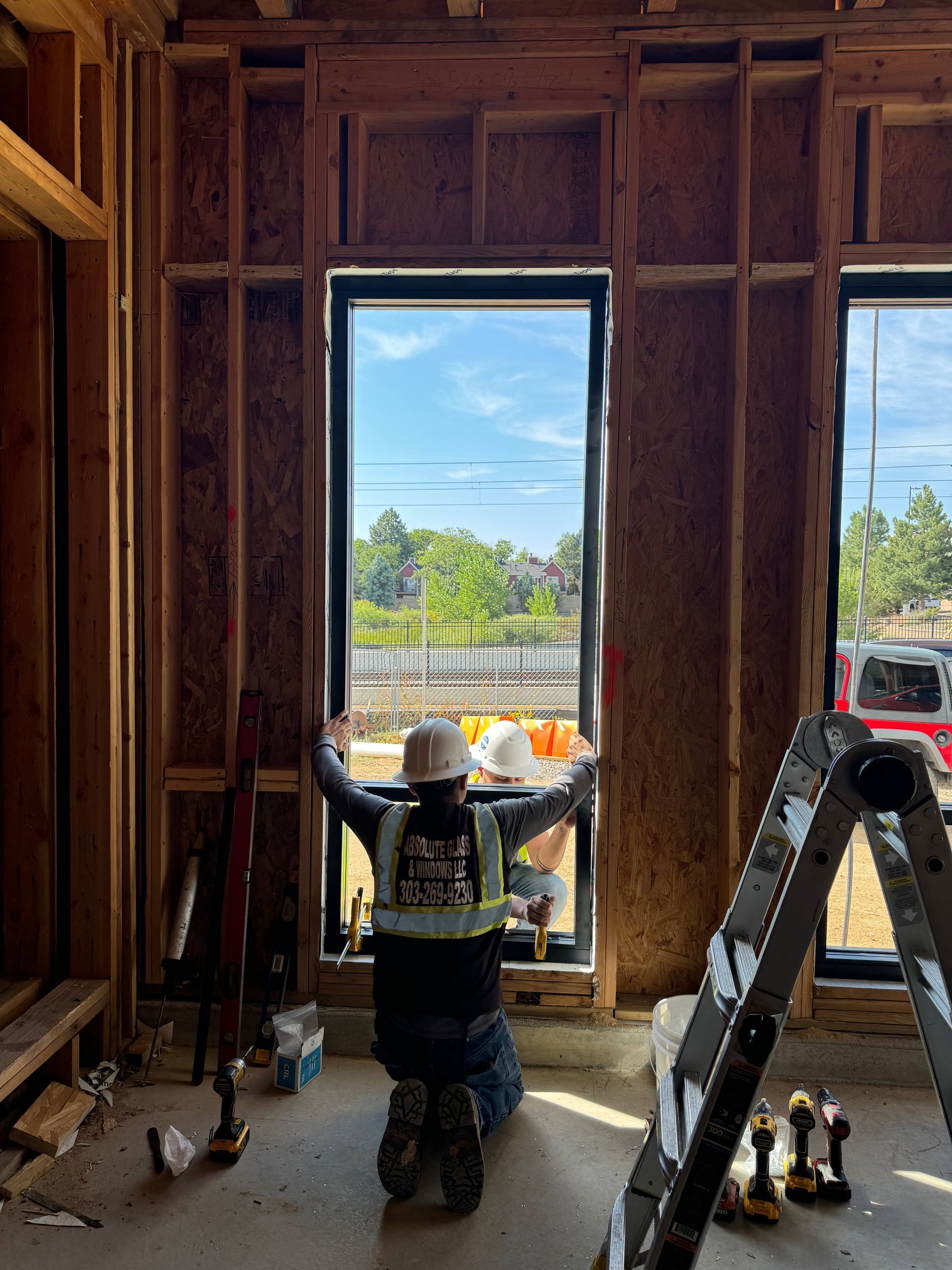 Construction worker installing window in a wood-framed wall. Bright sunny day.