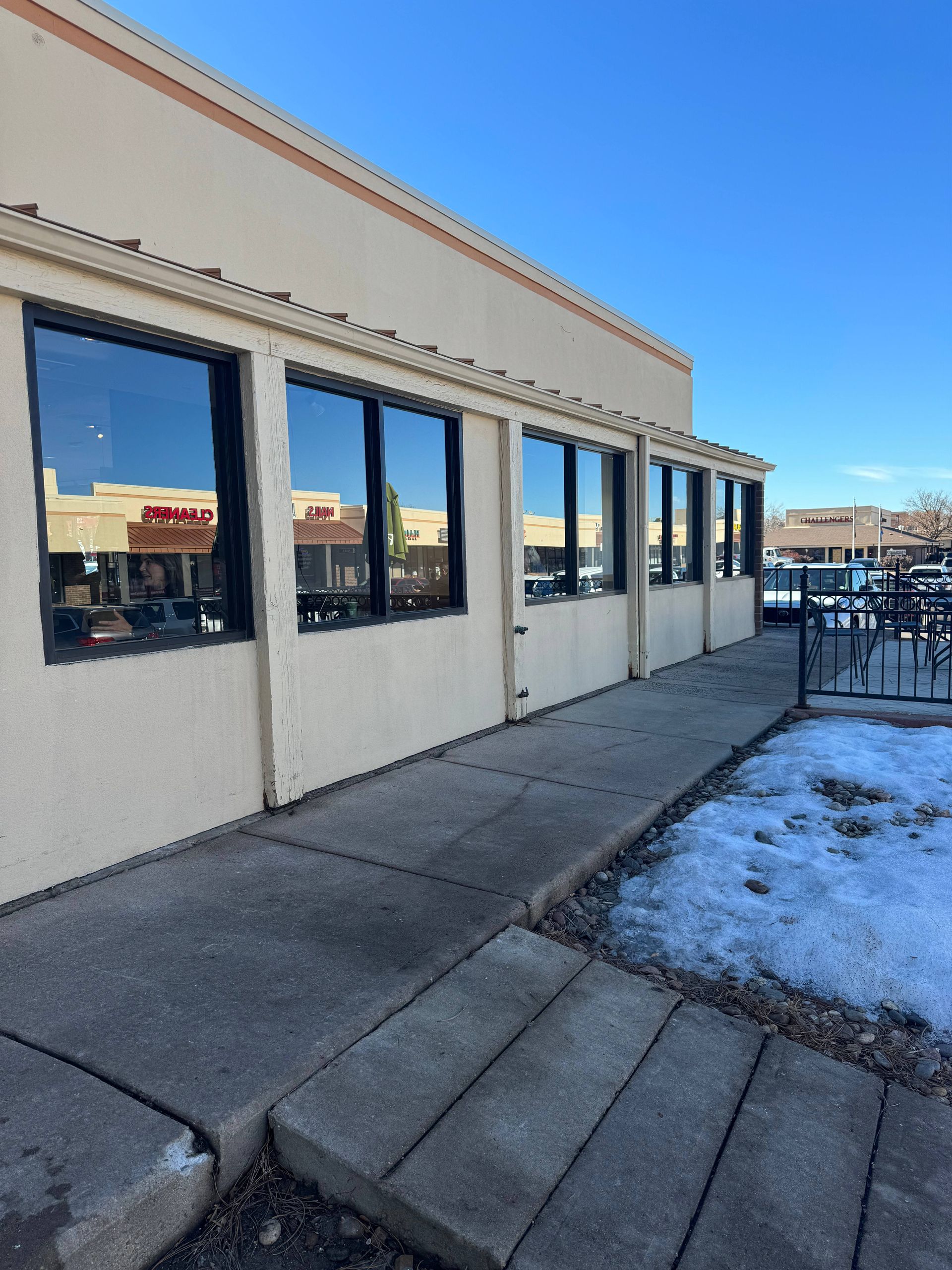 Exterior view of a building with large windows reflecting the sky, snow on the ground.