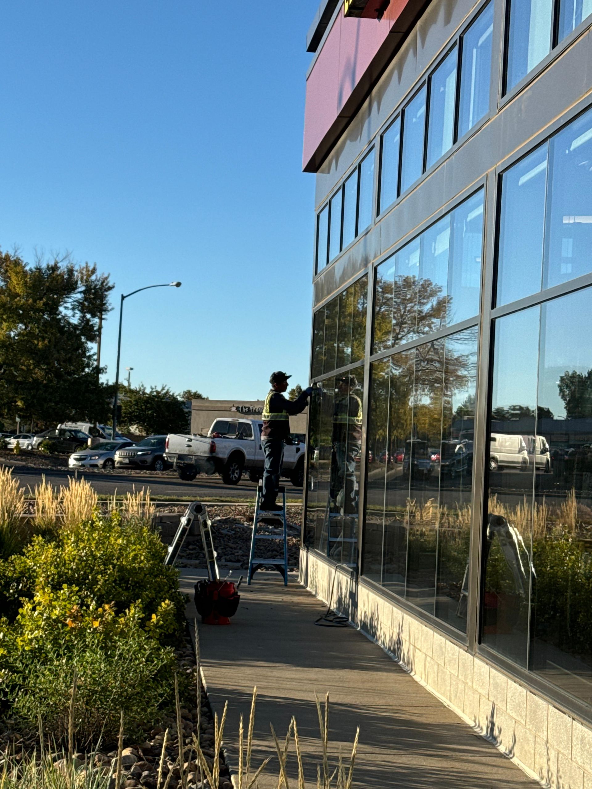 Person on ladder washing windows of a modern building on a sunny day.