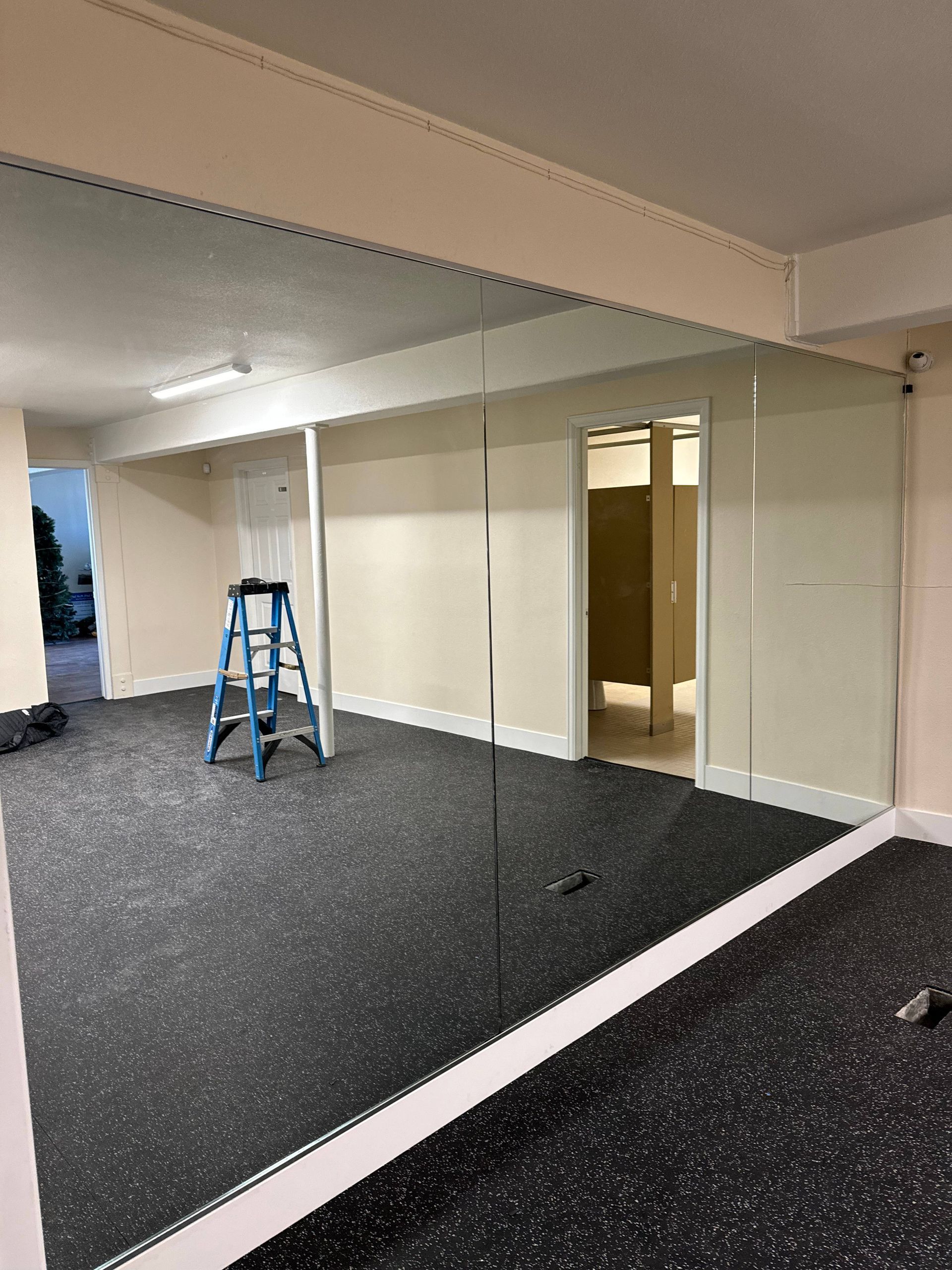 Gym interior with large mirror on wall, blue ladder, rubber floor, and neutral walls.