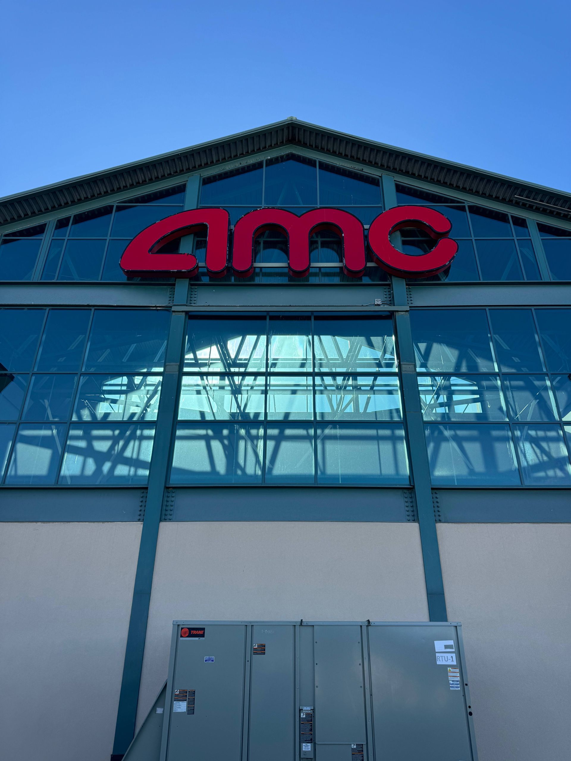 AMC movie theater with red logo against a blue sky and glass facade. Beige and gray building.