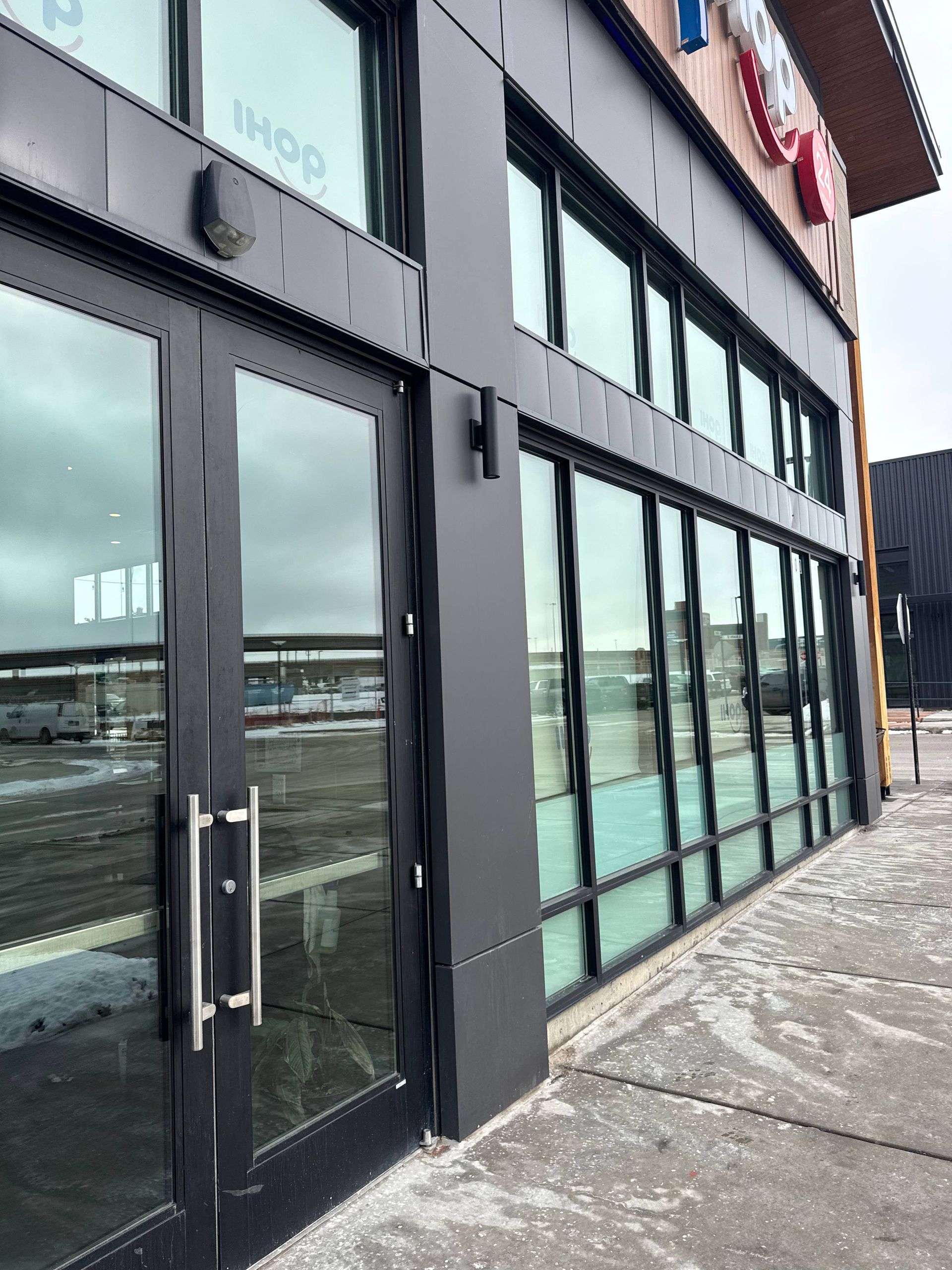 Black entrance to IHOP restaurant; glass doors, windows, and metal facade on a snowy day.