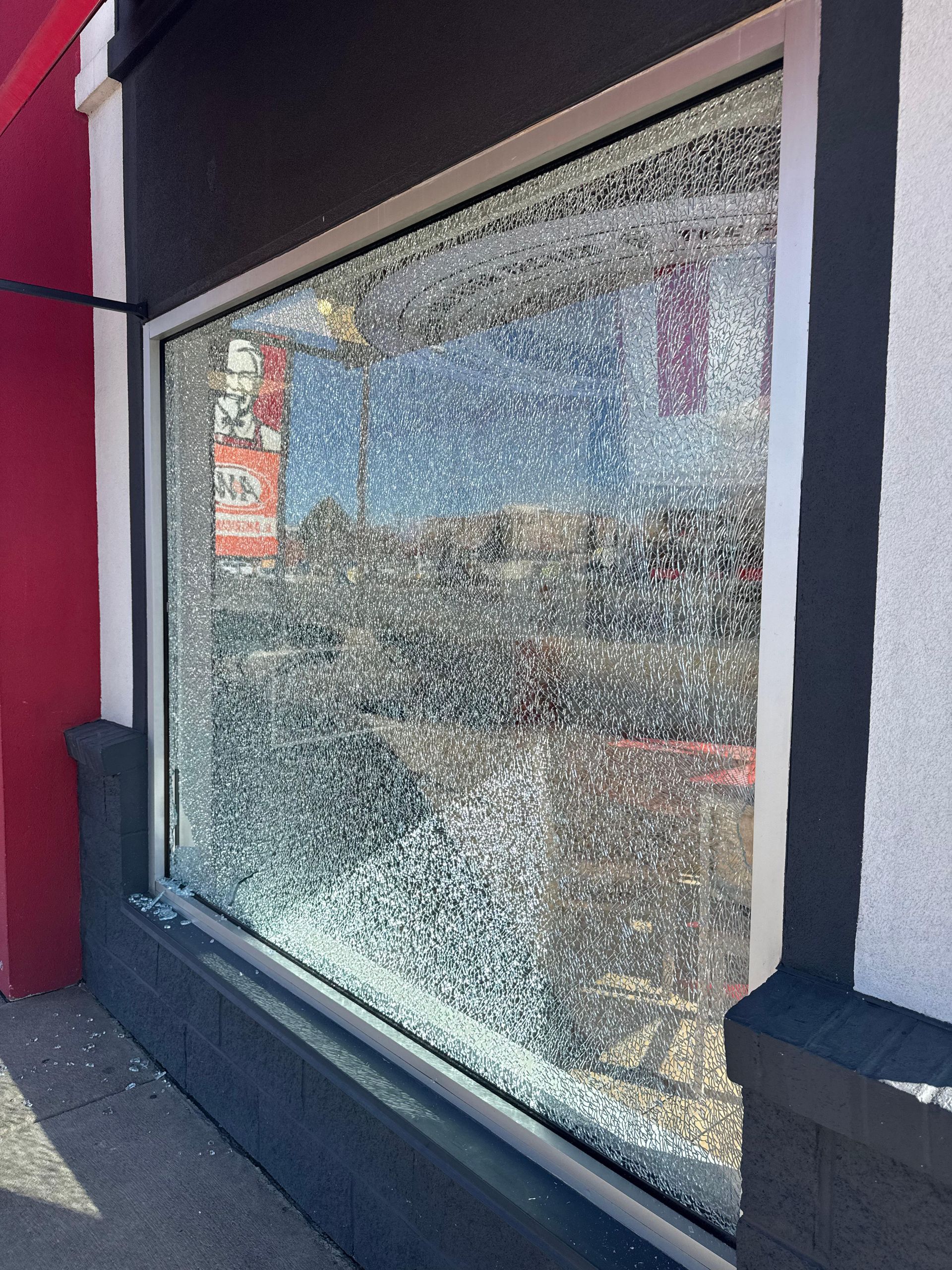 Shattered storefront window; glass fragments cover the pane. Building exterior: black, white, and red trim.