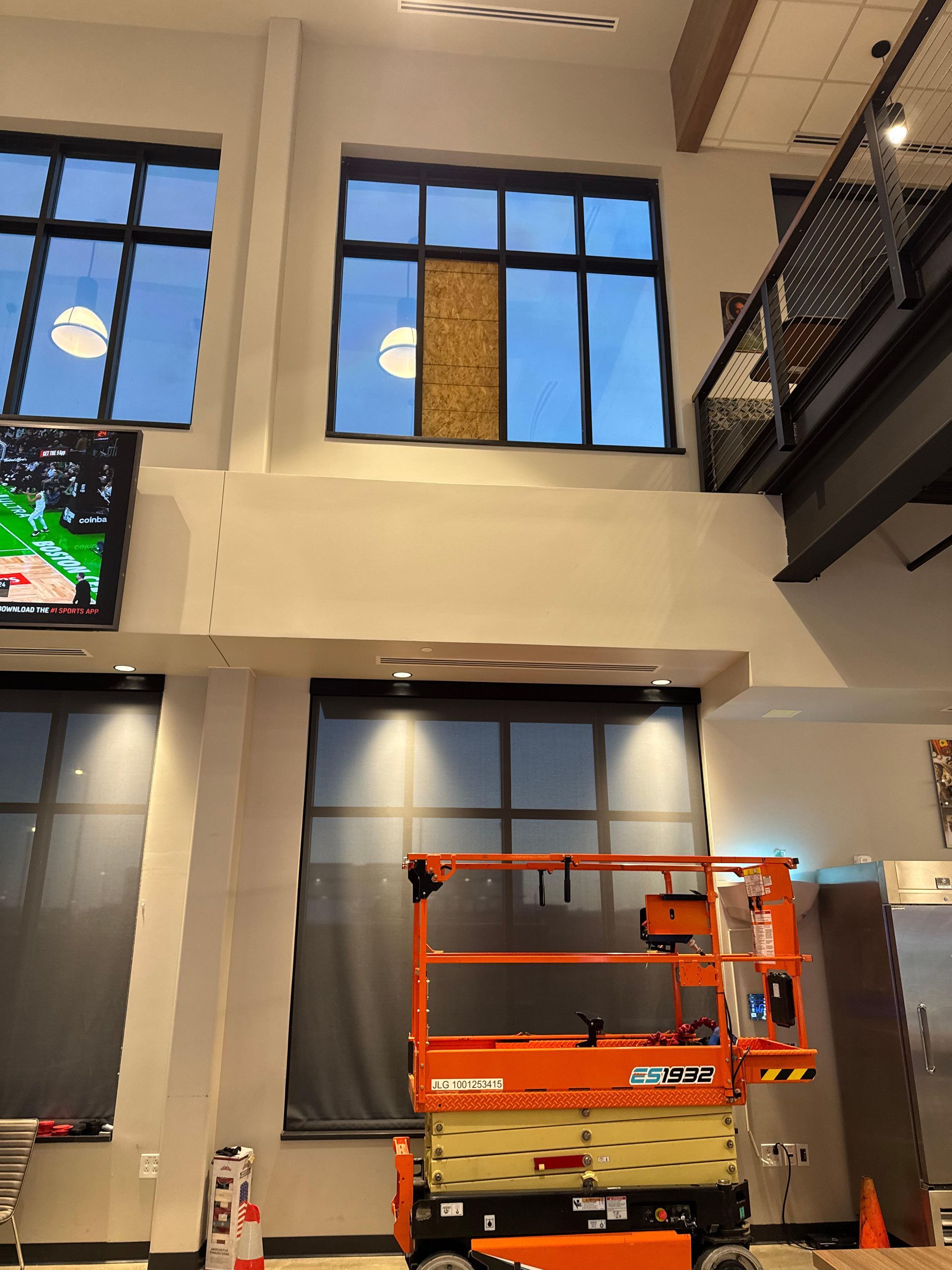 Interior: Lift platform near large windows, one boarded up. Basketball game on TV.